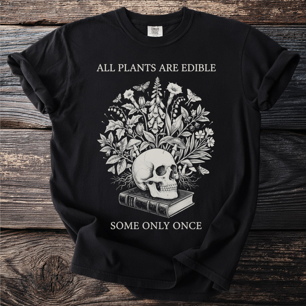 Black t-shirt with skull, book, plants, and moths. Text reads "ALL PLANTS ARE EDIBLE SOME ONLY ONCE".