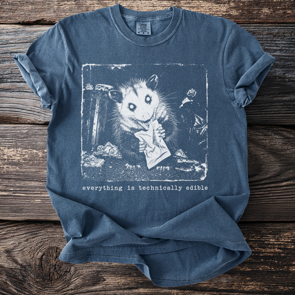 Blue t-shirt with a black and white graphic of an opossum eating from a wrapper surrounded by trash.