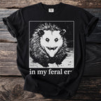 Black t-shirt with a graphic of a feral opossum and text "in my feral er".