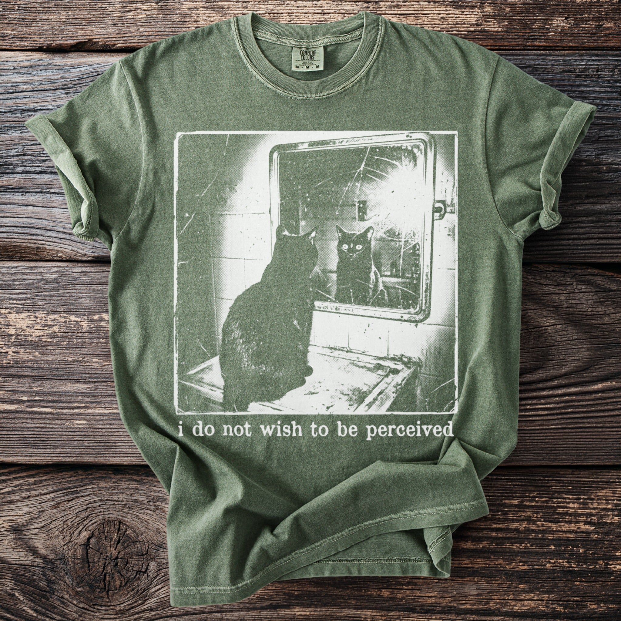 Green t-shirt with a cat looking in a cracked mirror and text "i do not wish to be perceived".