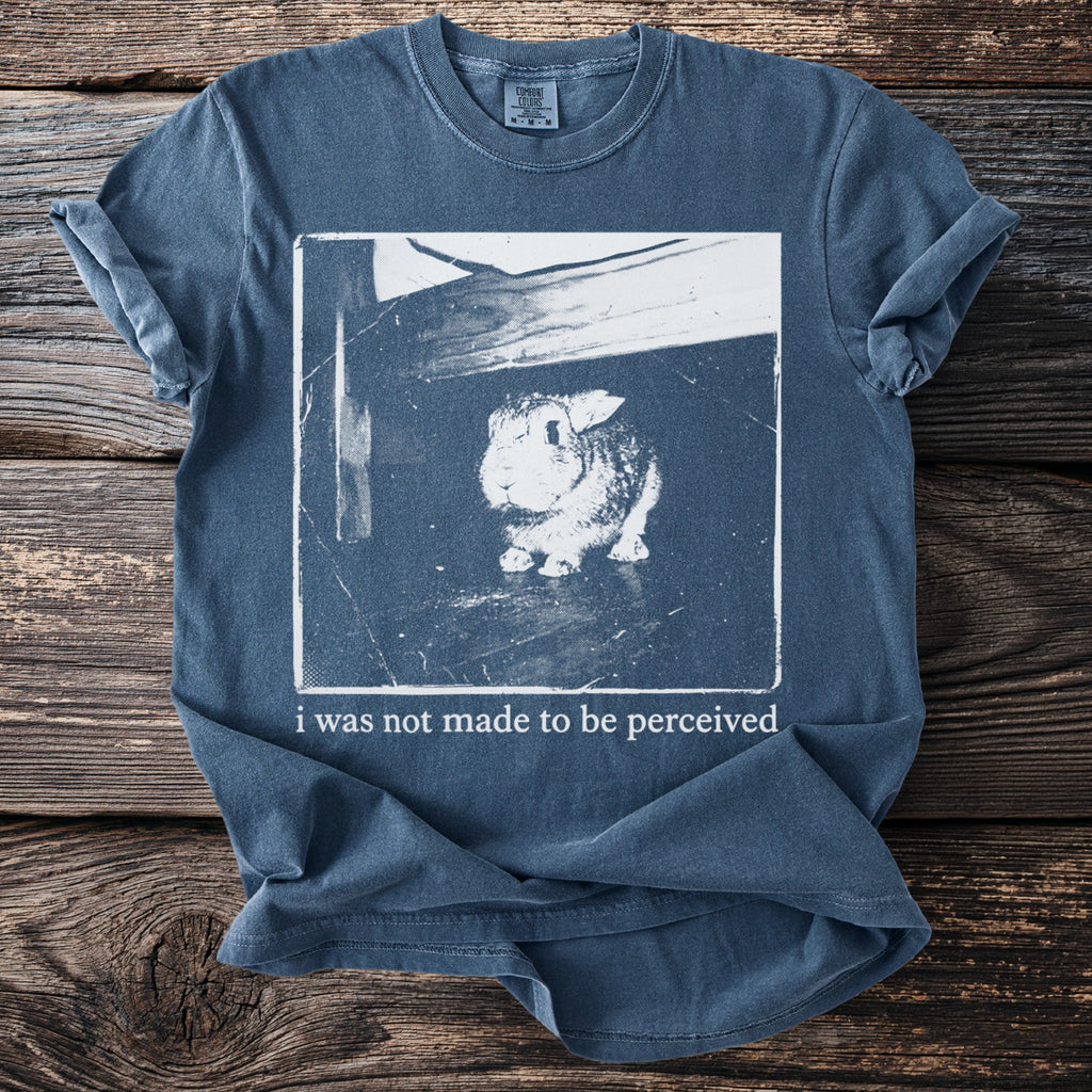 Blue t-shirt with a white graphic of a rabbit and the text "i was not made to be perceived."