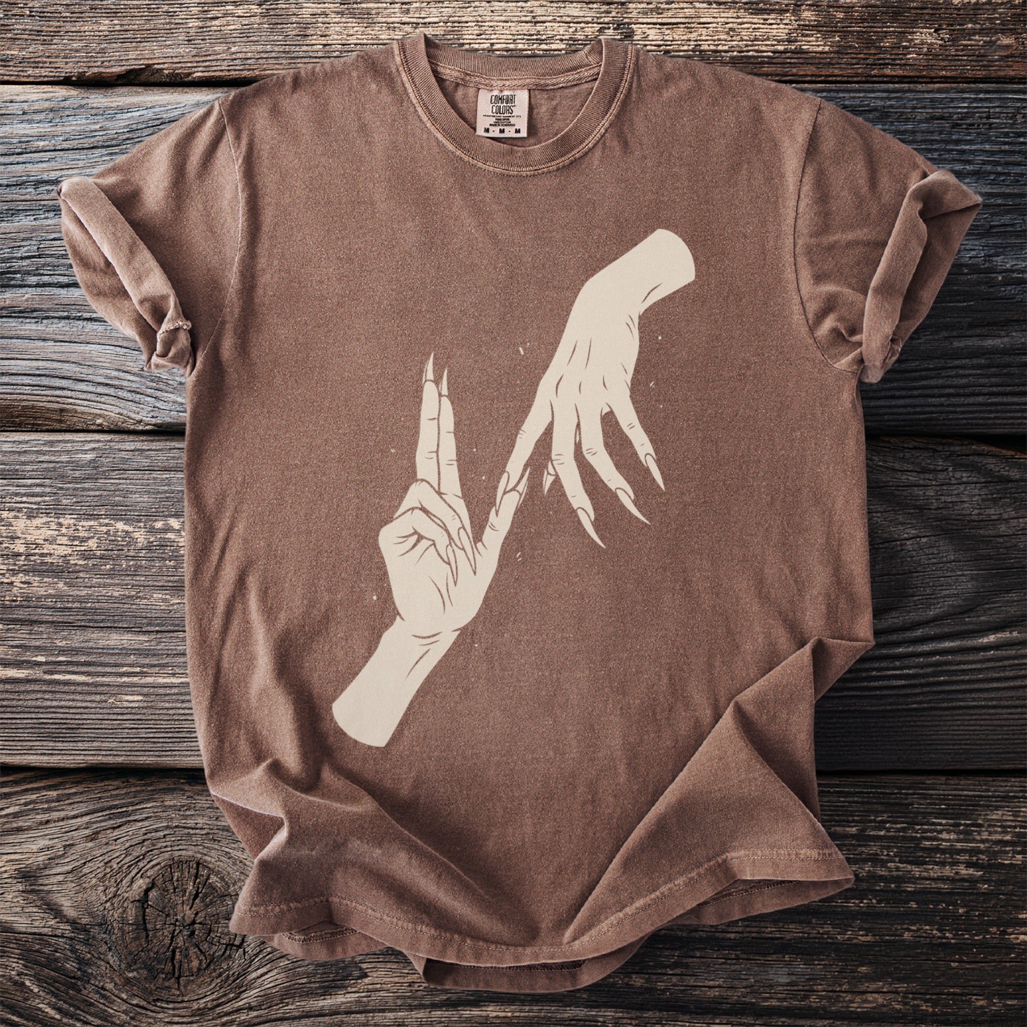 Brown t-shirt with a graphic of two hands with long, sharp fingernails.