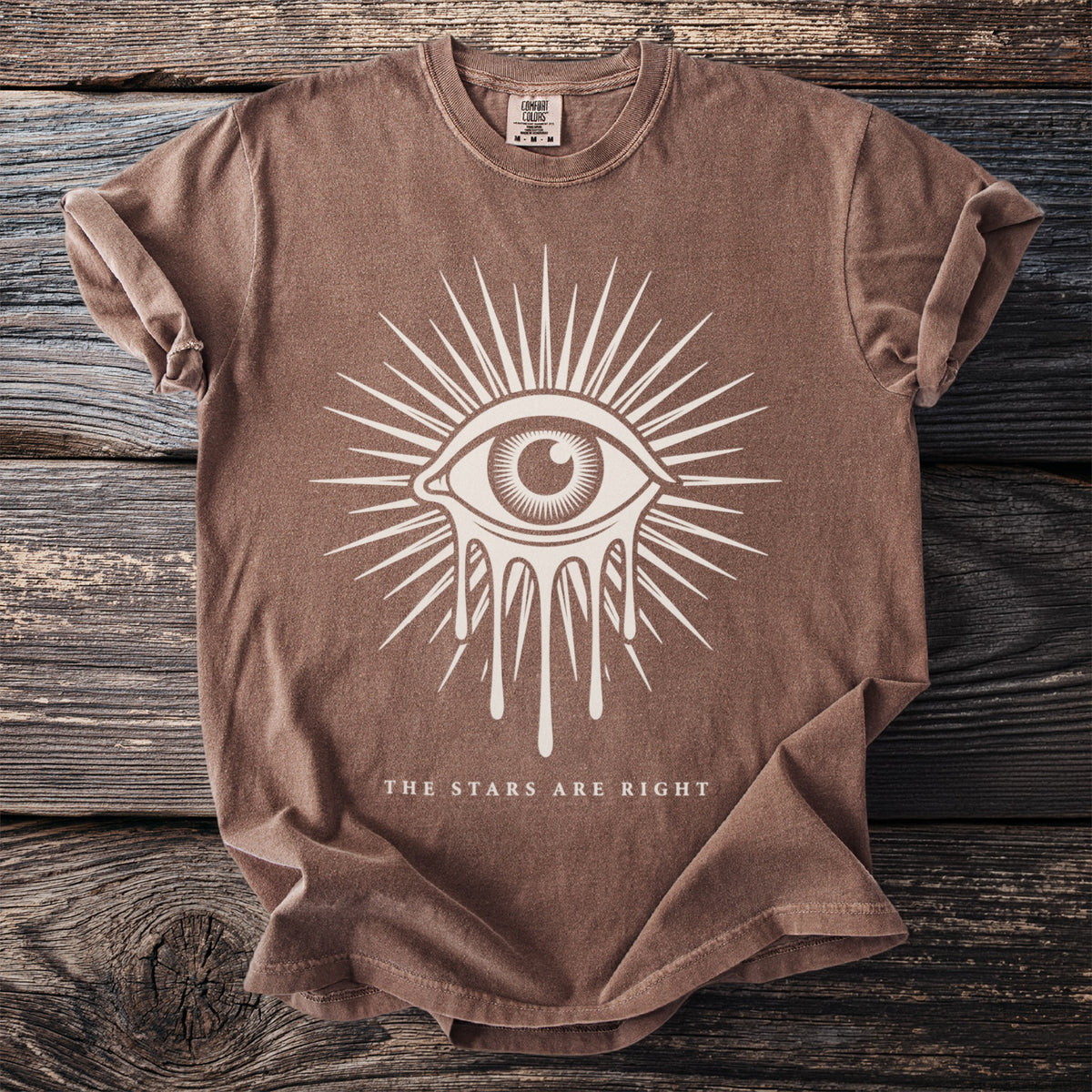 Brown t-shirt with white graphic of an eye with dripping tears and text "The Stars Are Right".