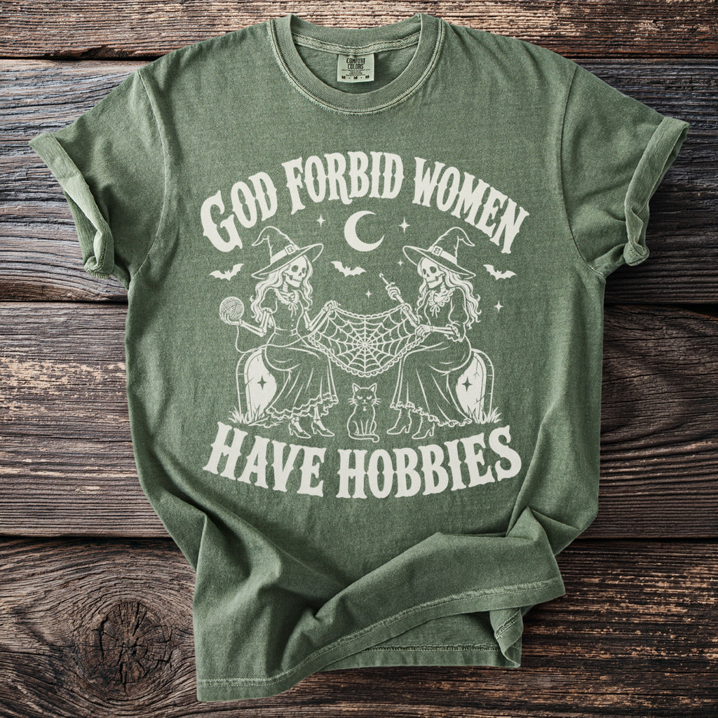Green t-shirt with "God Forbid Women Have Hobbies" text and witch skeletons knitting.