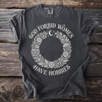 Dark grey t-shirt with "God Forbid Women Have Hobbies" text and floral moon design.