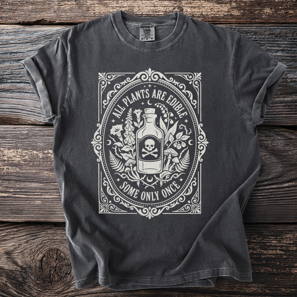 Dark gray t-shirt with white graphic of bottle, skull, and plants, text reads "ALL PLANTS ARE EDIBLE SOME ONLY ONCE".