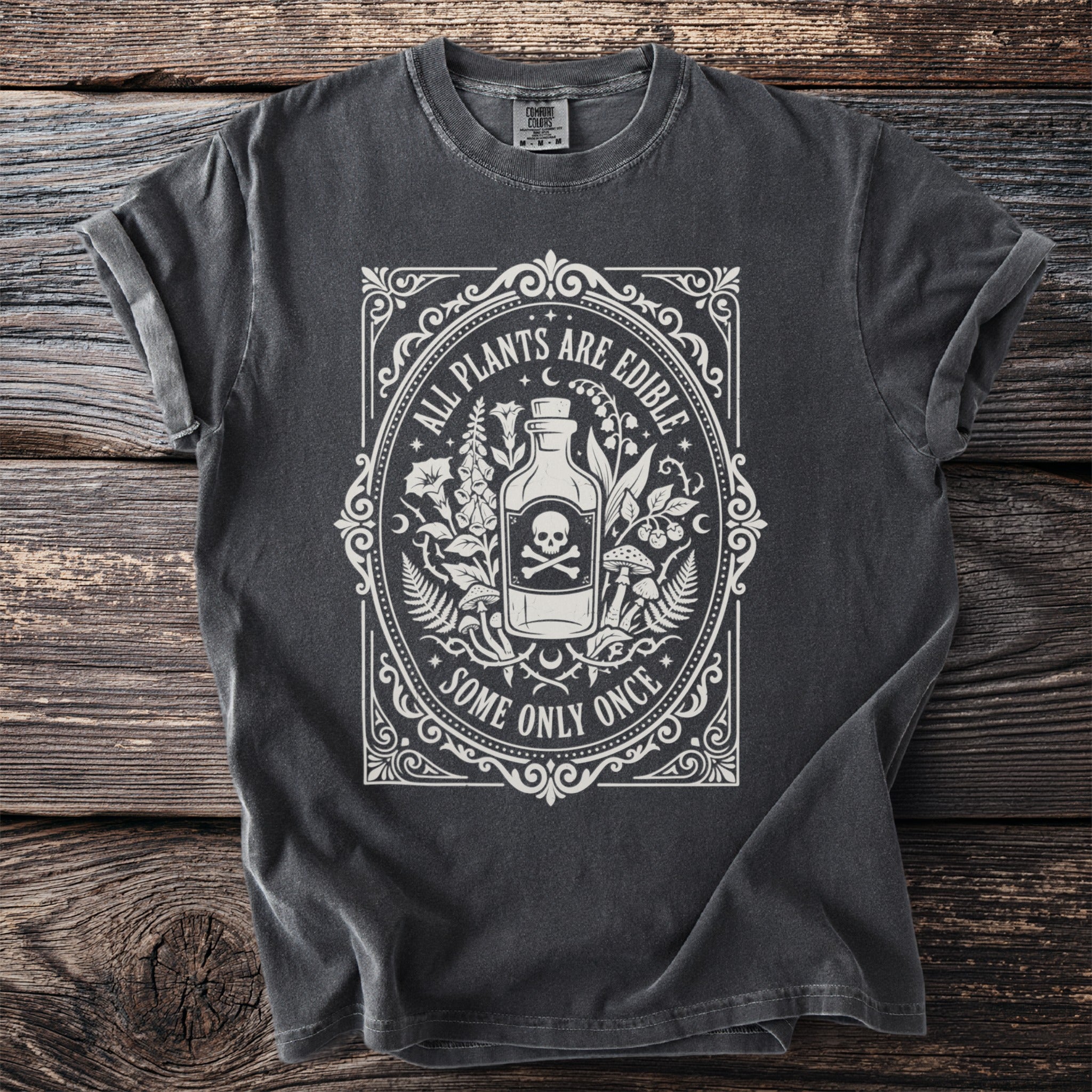 Dark gray t-shirt with white graphic of bottle, skull, and plants, text reads "ALL PLANTS ARE EDIBLE SOME ONLY ONCE".