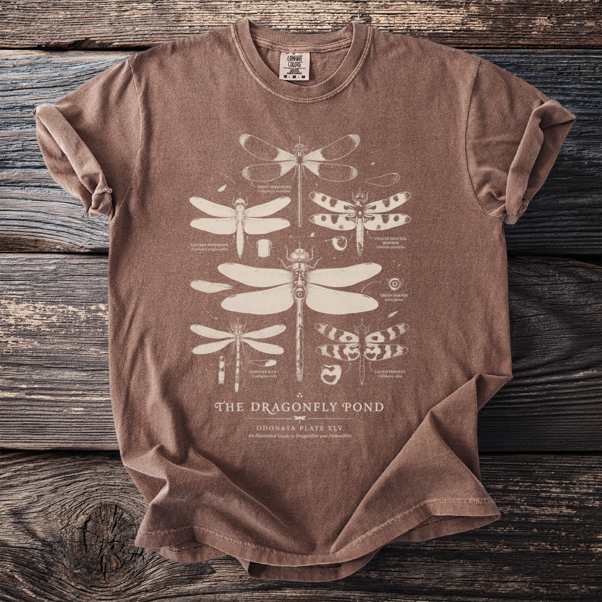 Brown t-shirt with beige dragonfly illustrations and text "The Dragonfly Pond".