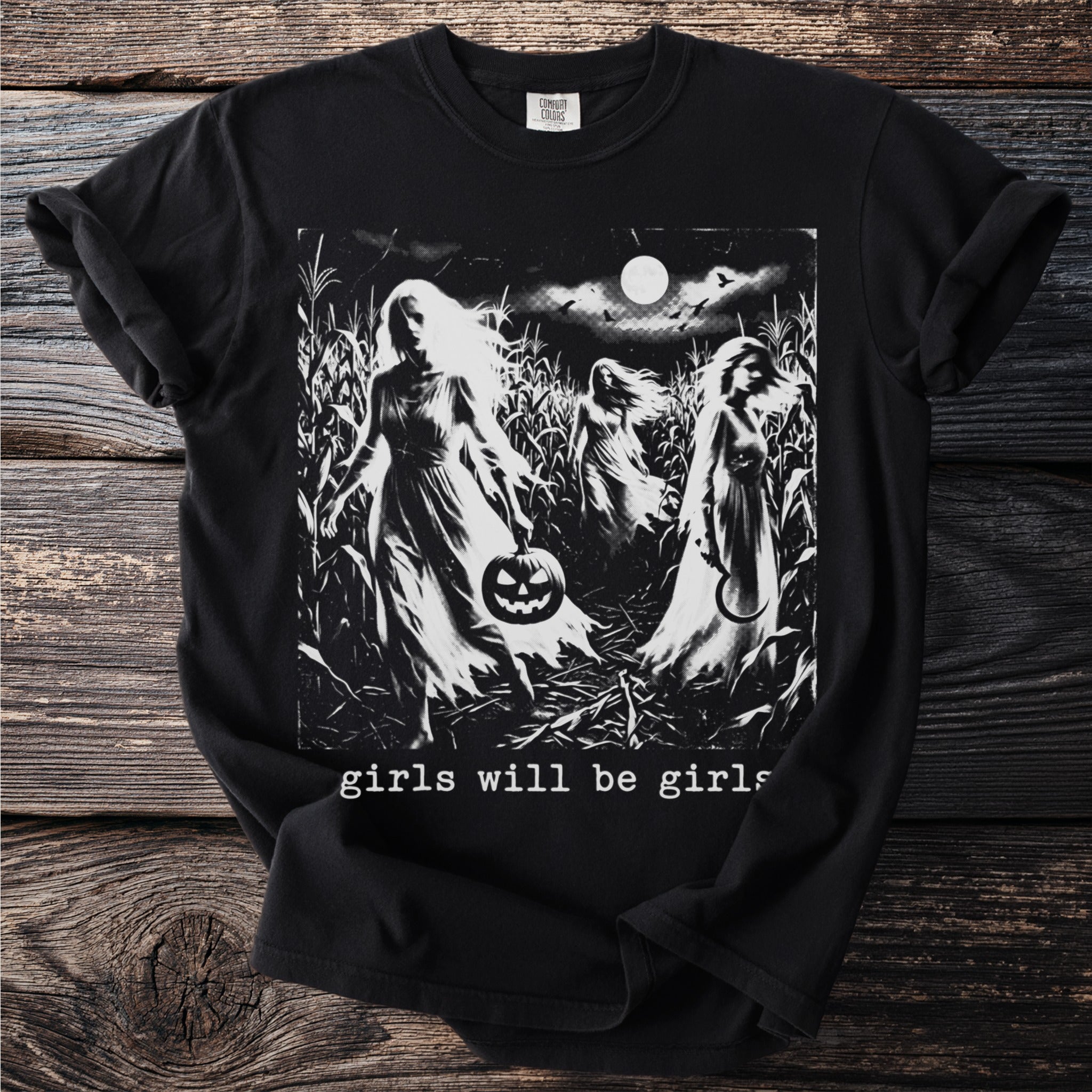 Black t-shirt with a print of spectral figures in a cornfield at night and the text "girls will be girls".