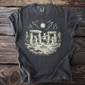 Dark gray t-shirt with three figures dancing around a fire inside a stone circle, the central one horned, a bright disc overhead.