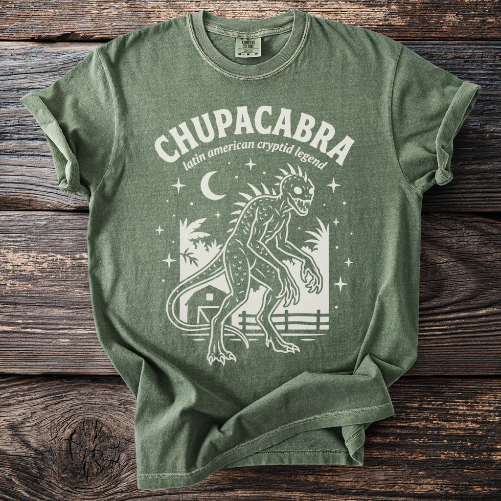 Green t-shirt with white graphic of a Chupacabra, moon, stars, and a barn.