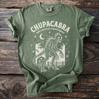 Green t-shirt with white graphic of a Chupacabra, moon, stars, and a barn.