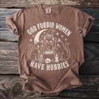 Brown shirt with white graphic of cats, cauldron, moon, and text "GOD FORBID WOMEN HAVE HOBBIES".