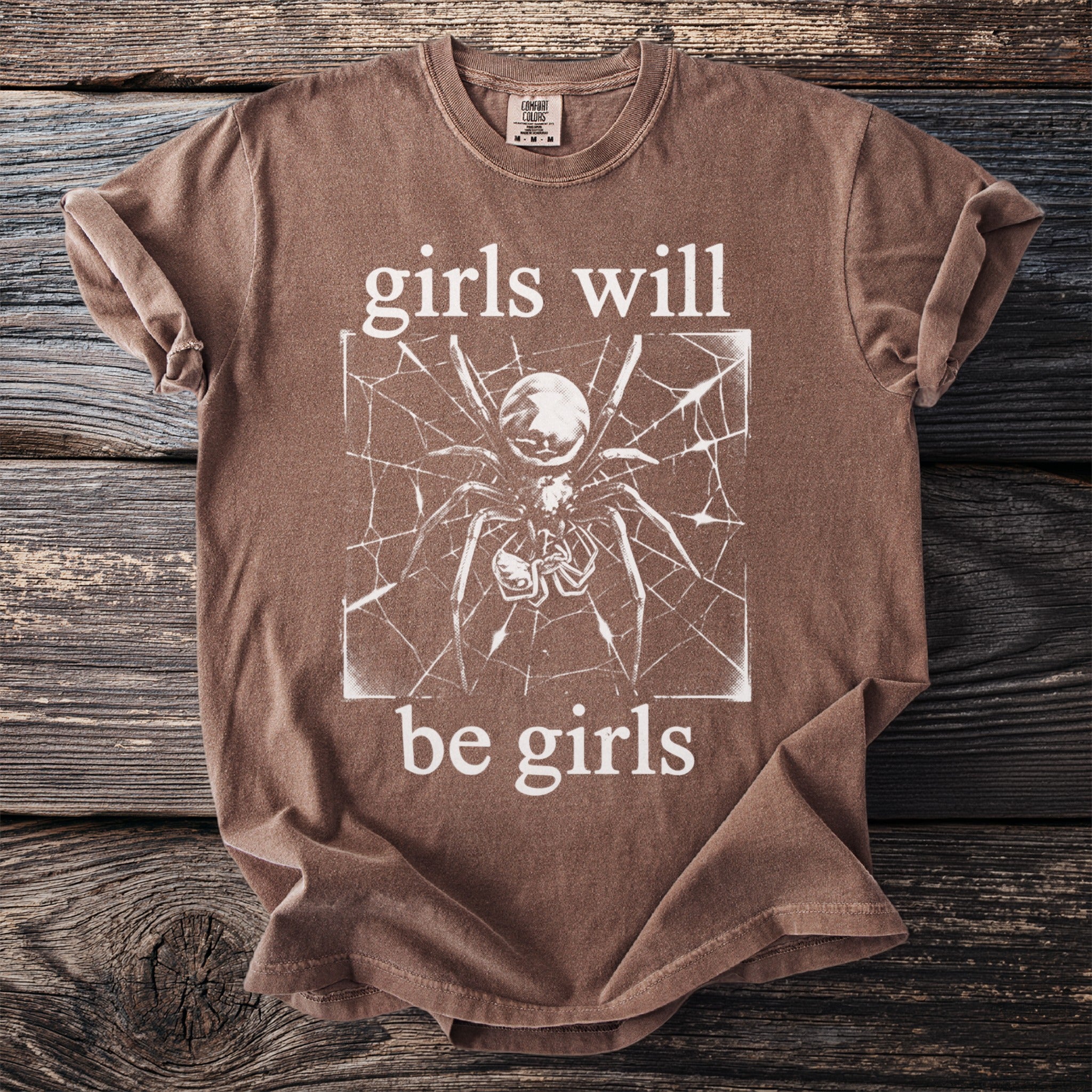 Brown t-shirt with white text "girls will be girls" and a spider graphic.