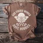 Brown t-shirt with "God forbid women have hobbies" text and moth graphic.