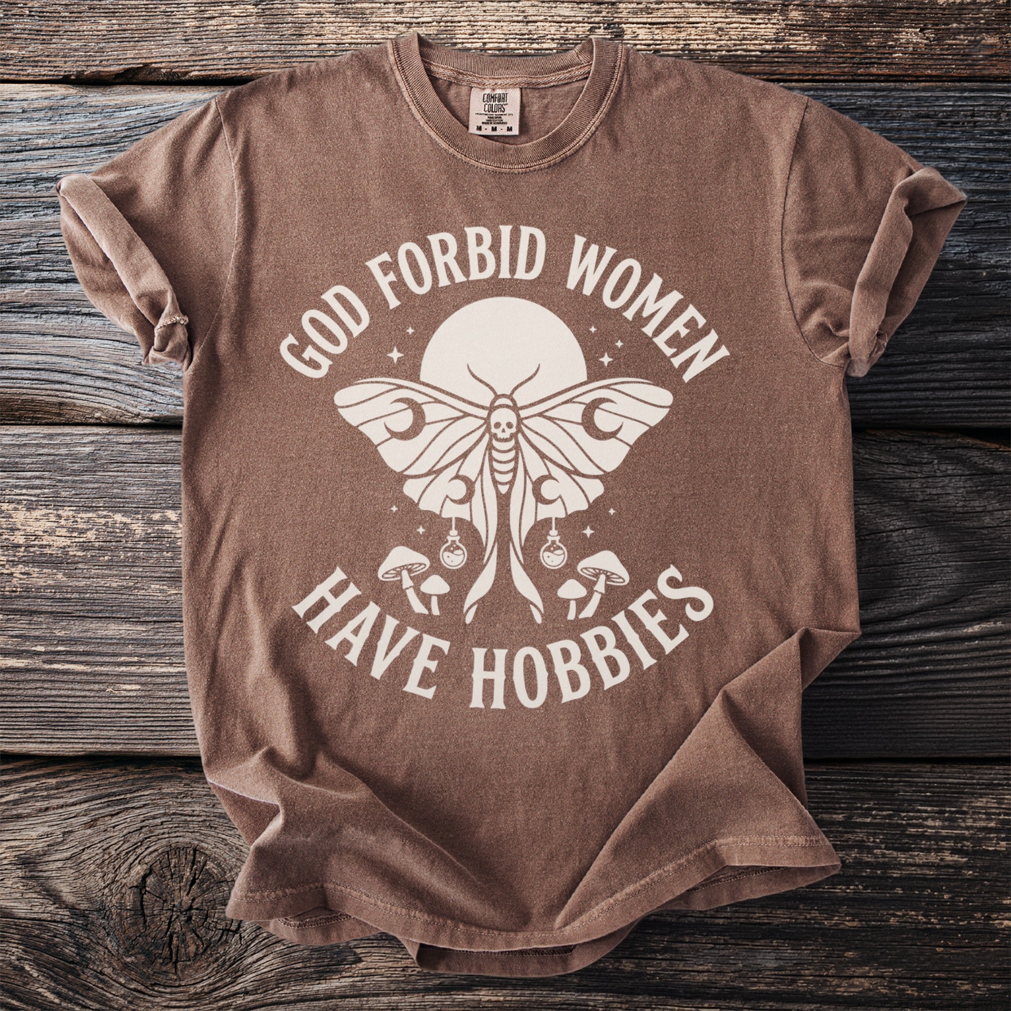 Brown t-shirt with "God forbid women have hobbies" text and moth graphic.