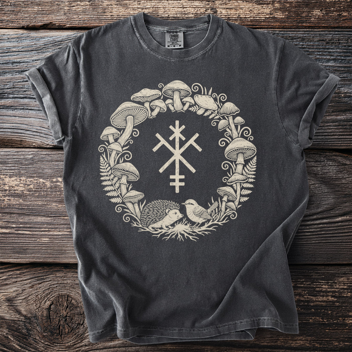 Dark grey t-shirt with a cream-colored circular print of mushrooms, ferns, a hedgehog, a bird, and a symbol.