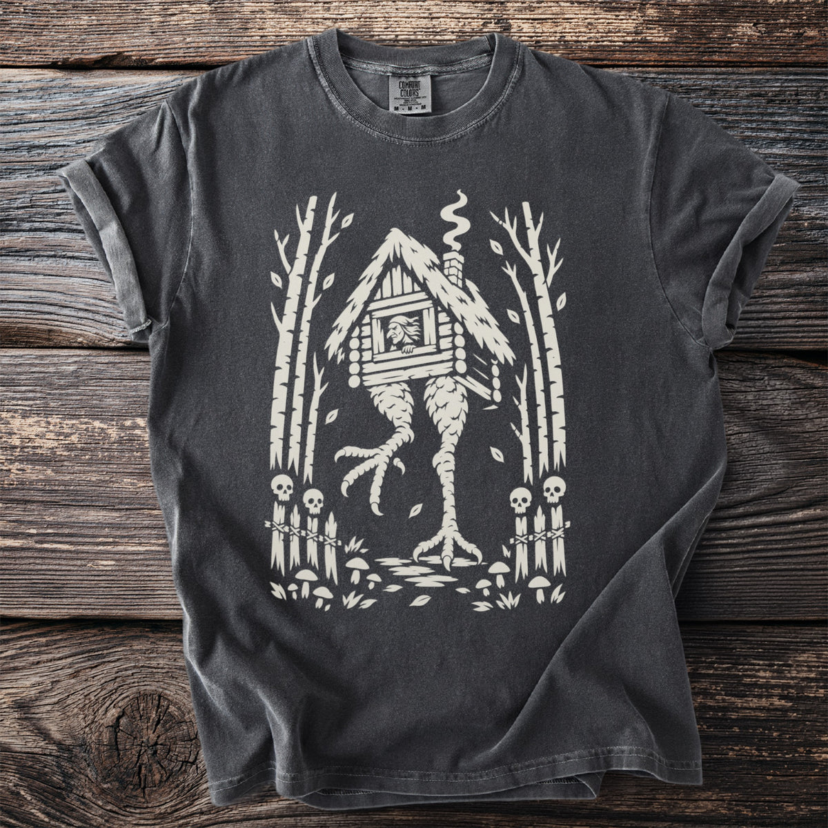 T-shirt with a cream graphic of a hut on chicken legs in a forest.