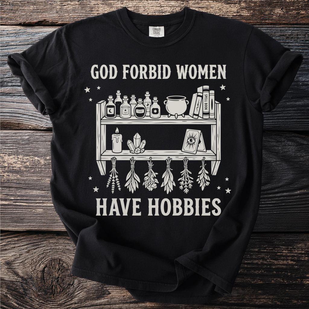 Black t-shirt with white text reading "GOD FORBID WOMEN HAVE HOBBIES" and a graphic of a shelf.