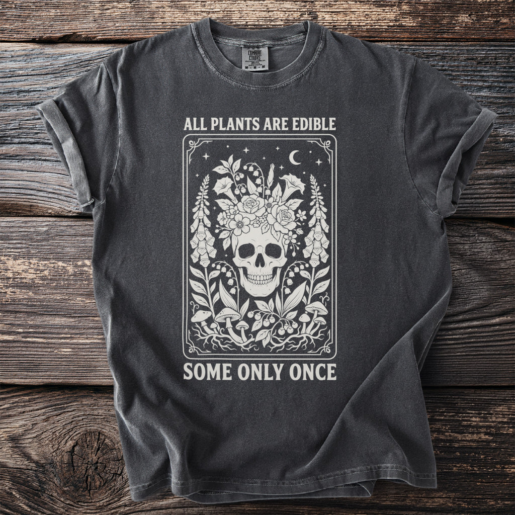 Dark grey t-shirt with skull, flowers, mushrooms, and text "ALL PLANTS ARE EDIBLE SOME ONLY ONCE".