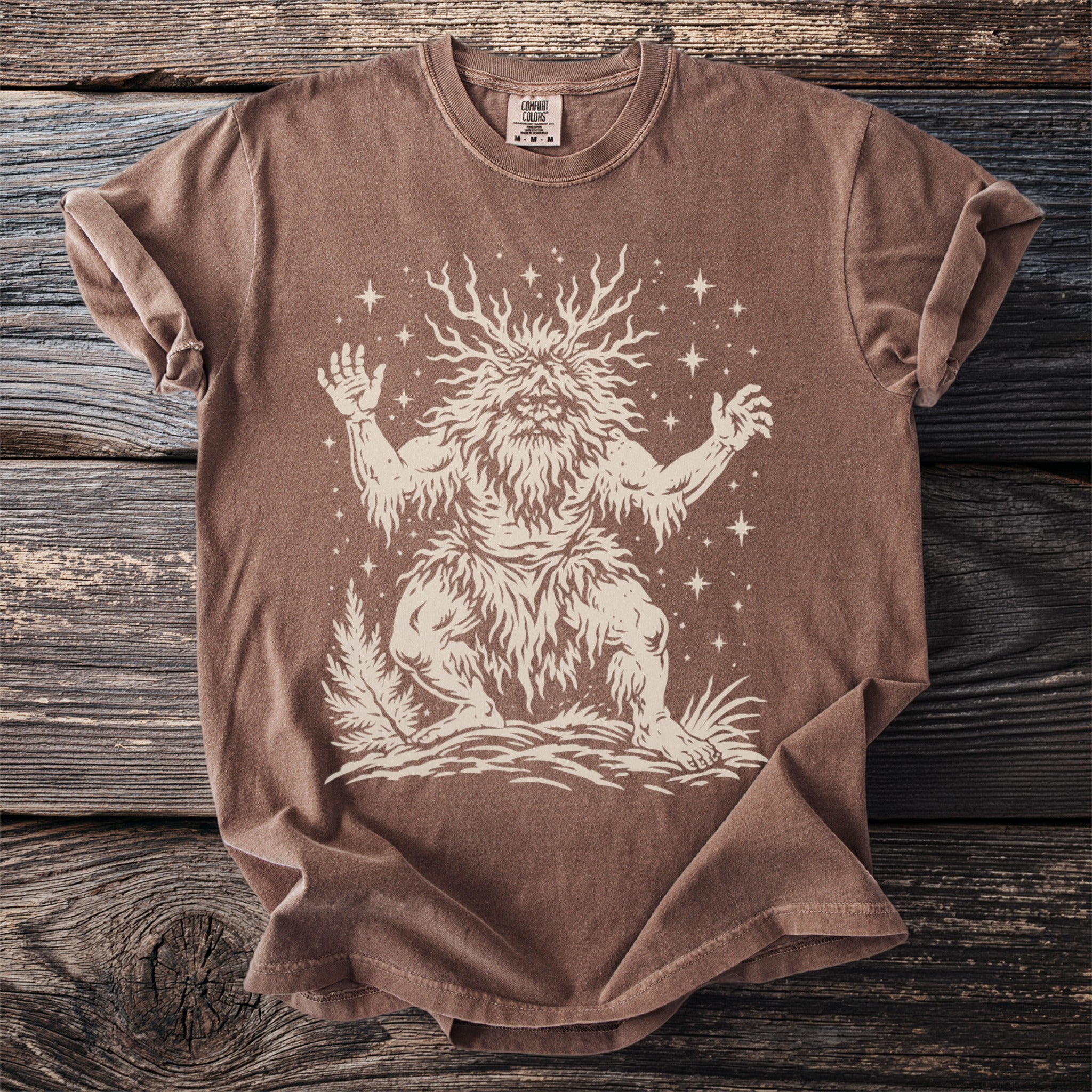 Brown t-shirt with a cream illustration of a horned, bearded creature surrounded by stars.