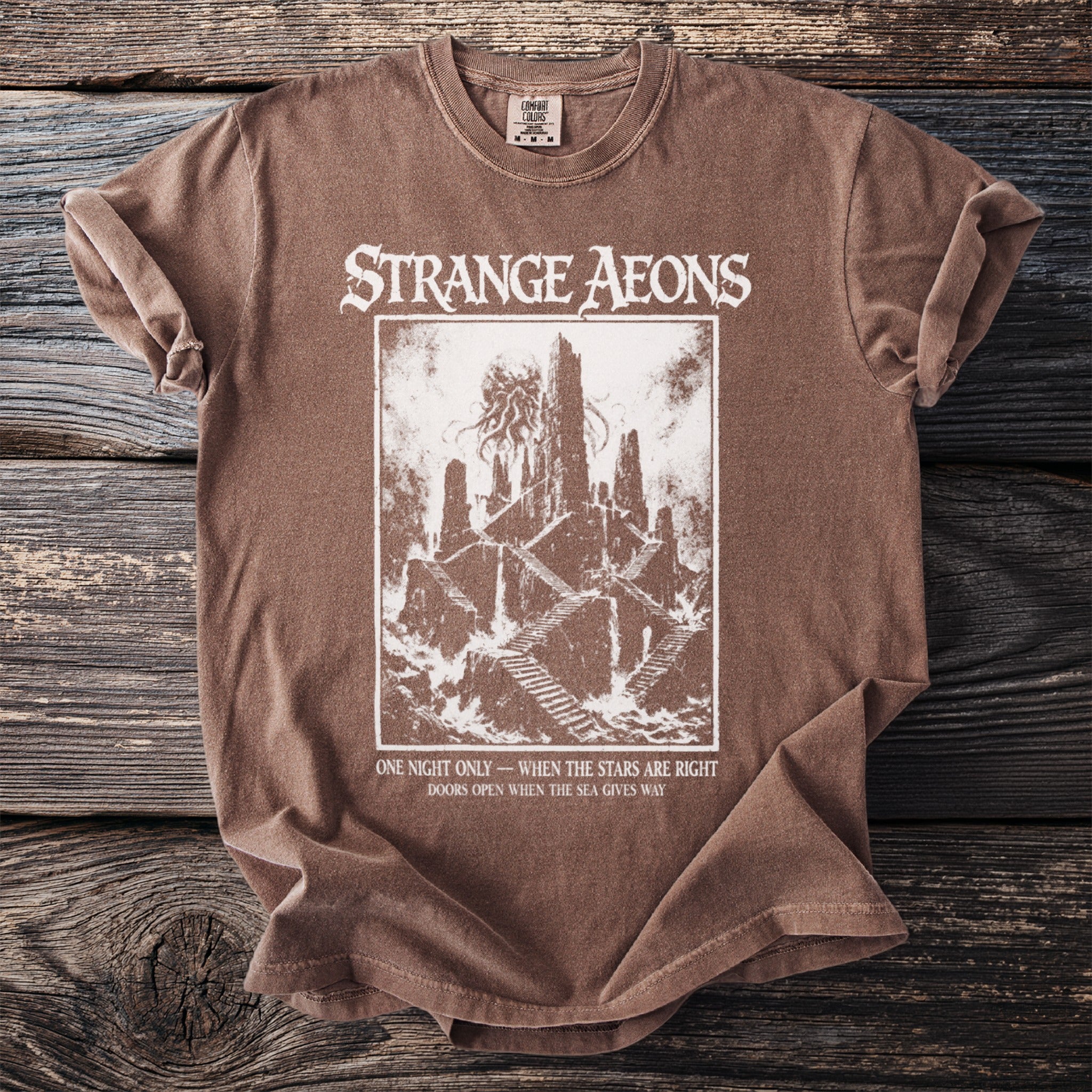 Brown t-shirt with "STRANGE AEONS" text and a cosmic horror illustration.
