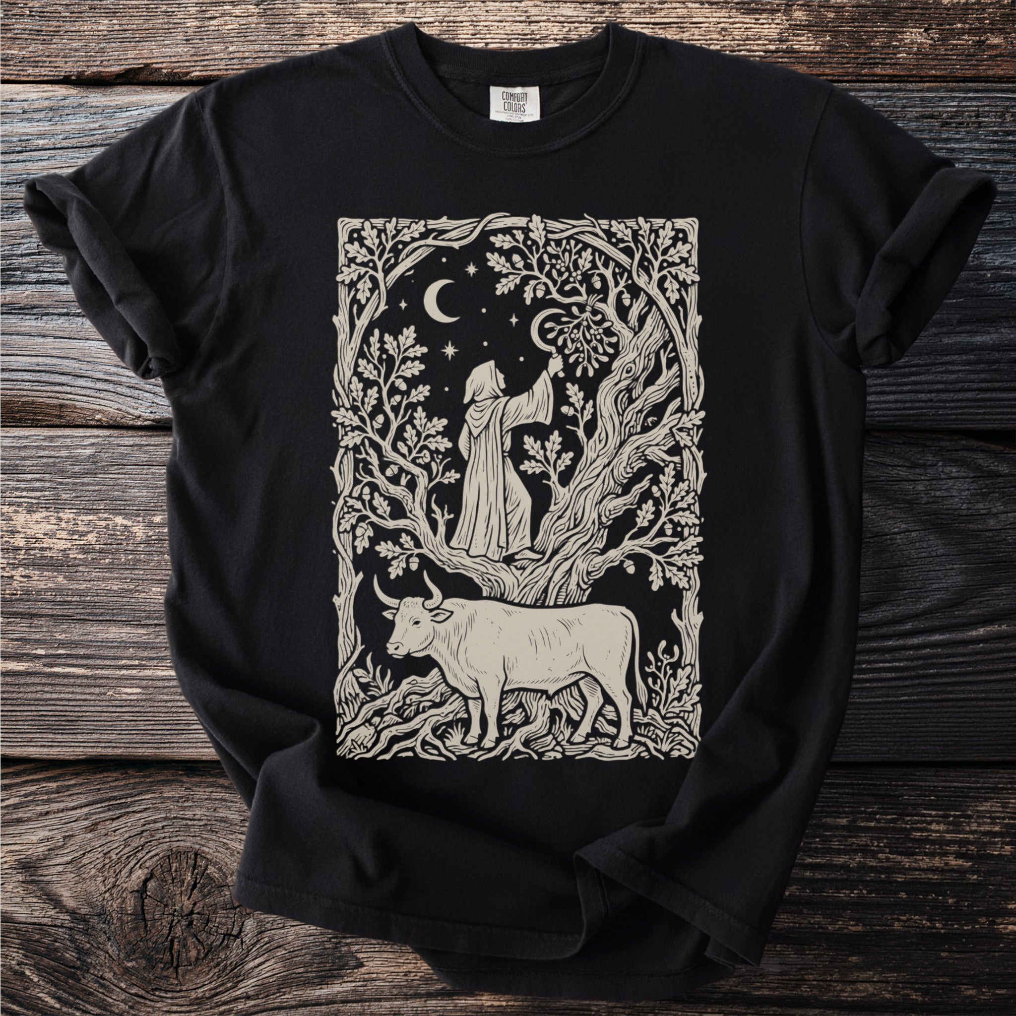 T-shirt with a black print of a robed figure and a bull in a stylized forest under a crescent moon.