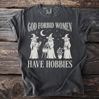 Dark grey t-shirt with "God Forbid Women Have Hobbies" and witch graphics.