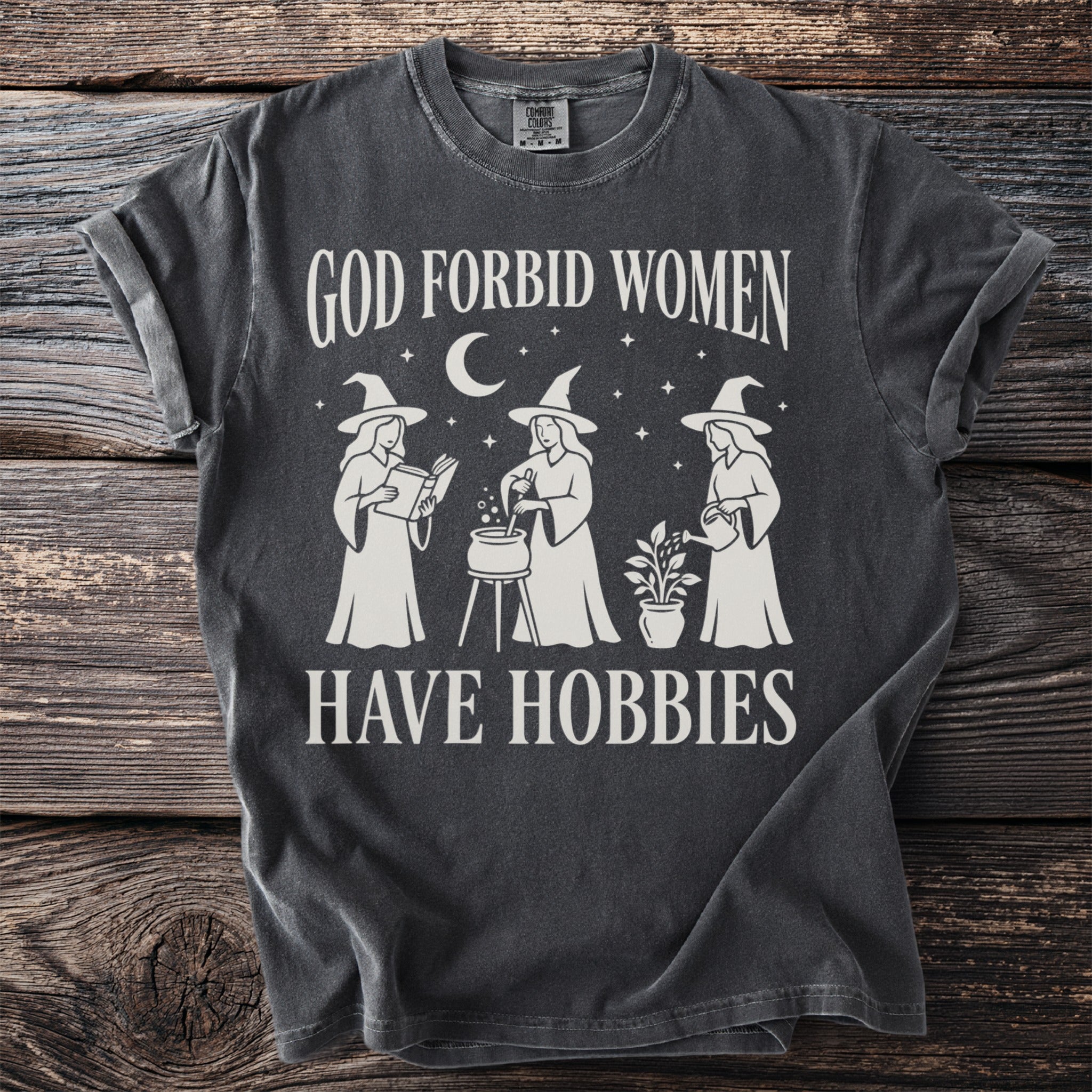 Dark grey t-shirt with "God Forbid Women Have Hobbies" and witch graphics.