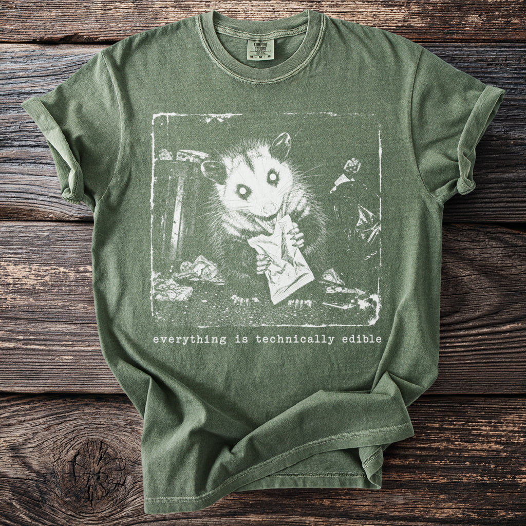Green t-shirt with white print of a possum eating from a bag, saying "everything is technically edible".