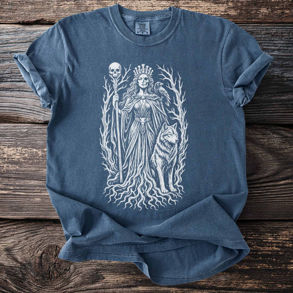 White graphic of a crowned queen with a skull staff, wolf, and raven on a blue t-shirt.