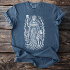 White graphic of a crowned queen with a skull staff, wolf, and raven on a blue t-shirt.