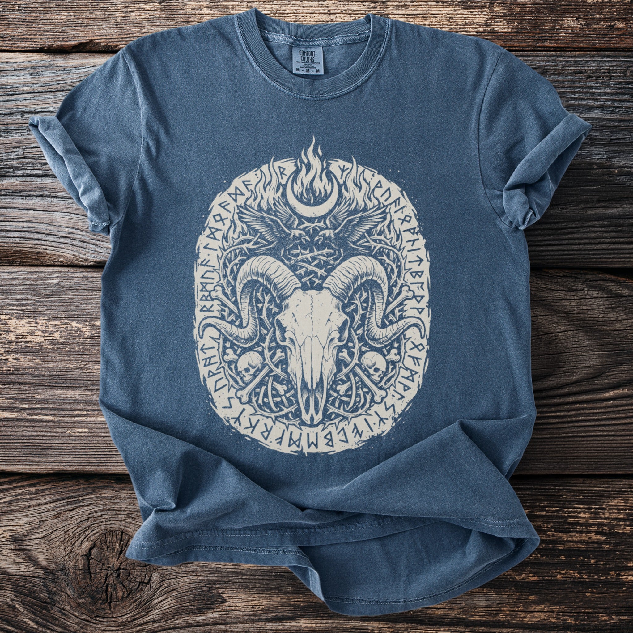 Blue t-shirt with a central oval graphic of a ram skull, wings, and runes.