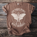 Brown t-shirt with white moth graphic and text "God Forbid Women Have Hobbies".