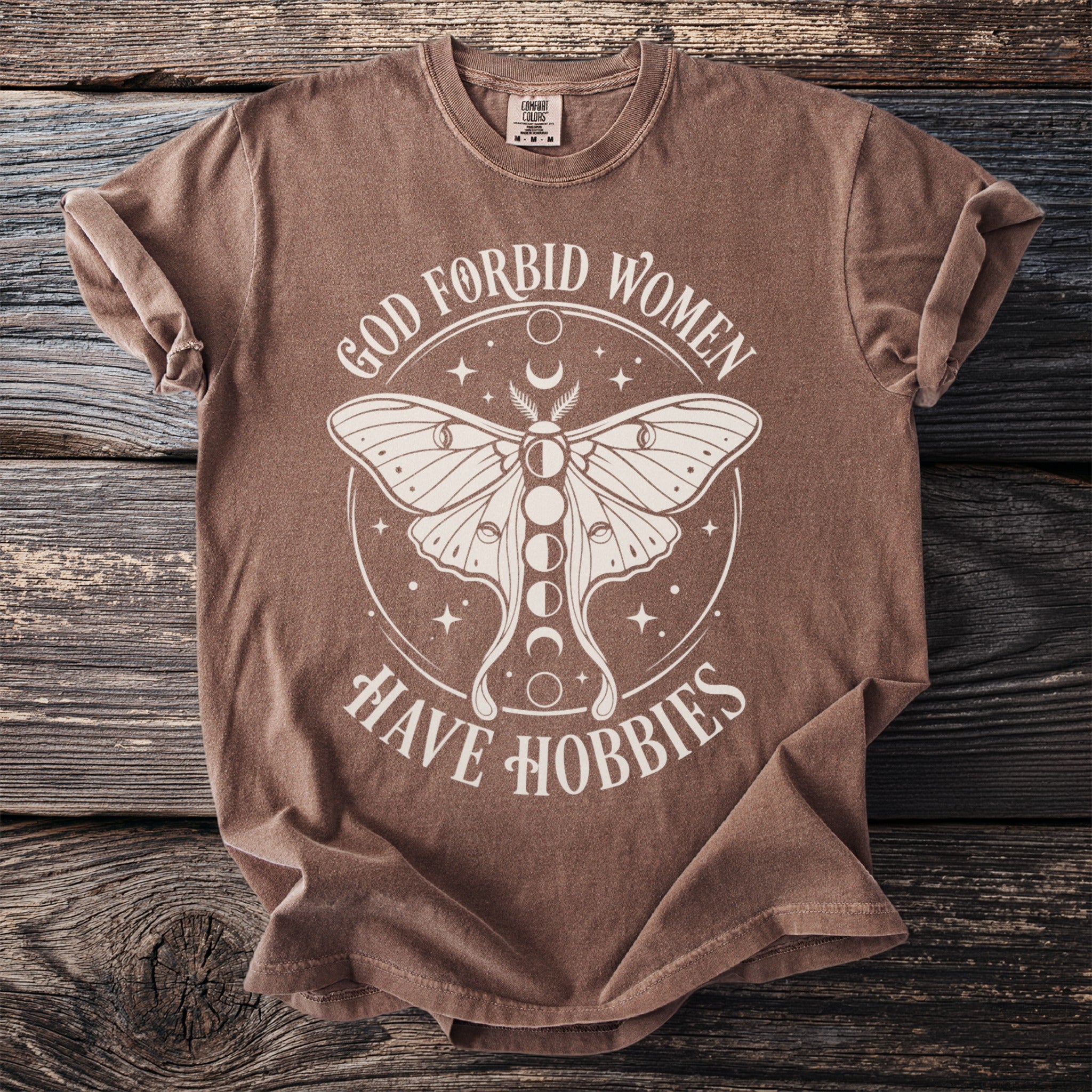 Brown t-shirt with white moth graphic and text "God Forbid Women Have Hobbies".