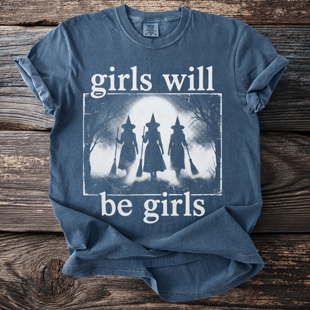 Blue t-shirt with white text "girls will be girls" and a graphic of three witches.