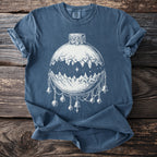 Blue t-shirt with white line art of a moon as a landscape containing mountains with bells and ornaments.