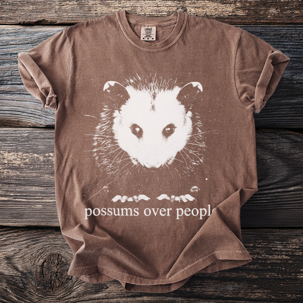 Brown t-shirt with white opossum graphic and text "possums over people".