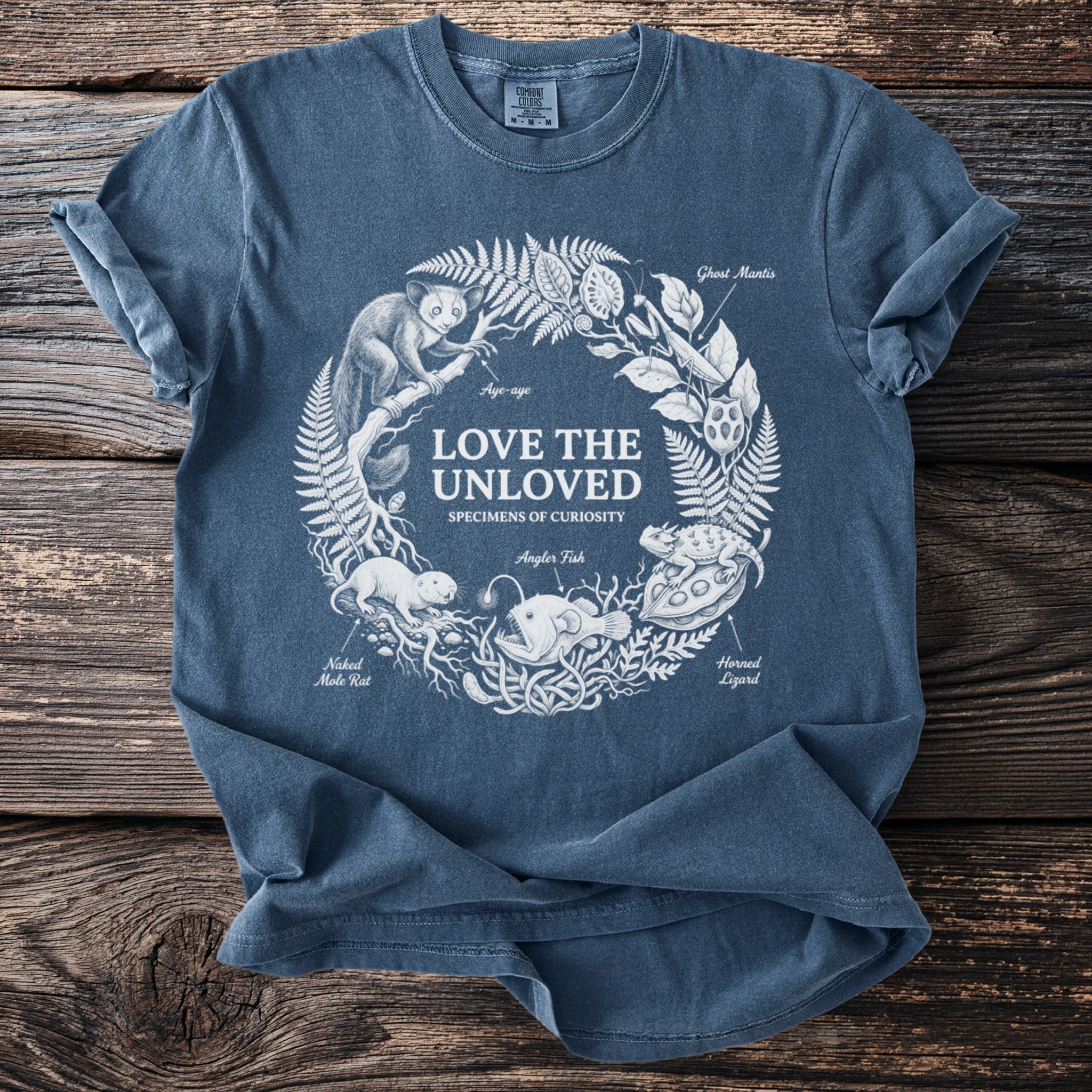 Blue t-shirt with "Love the Unloved" and illustrations of odd creatures in a circular design.