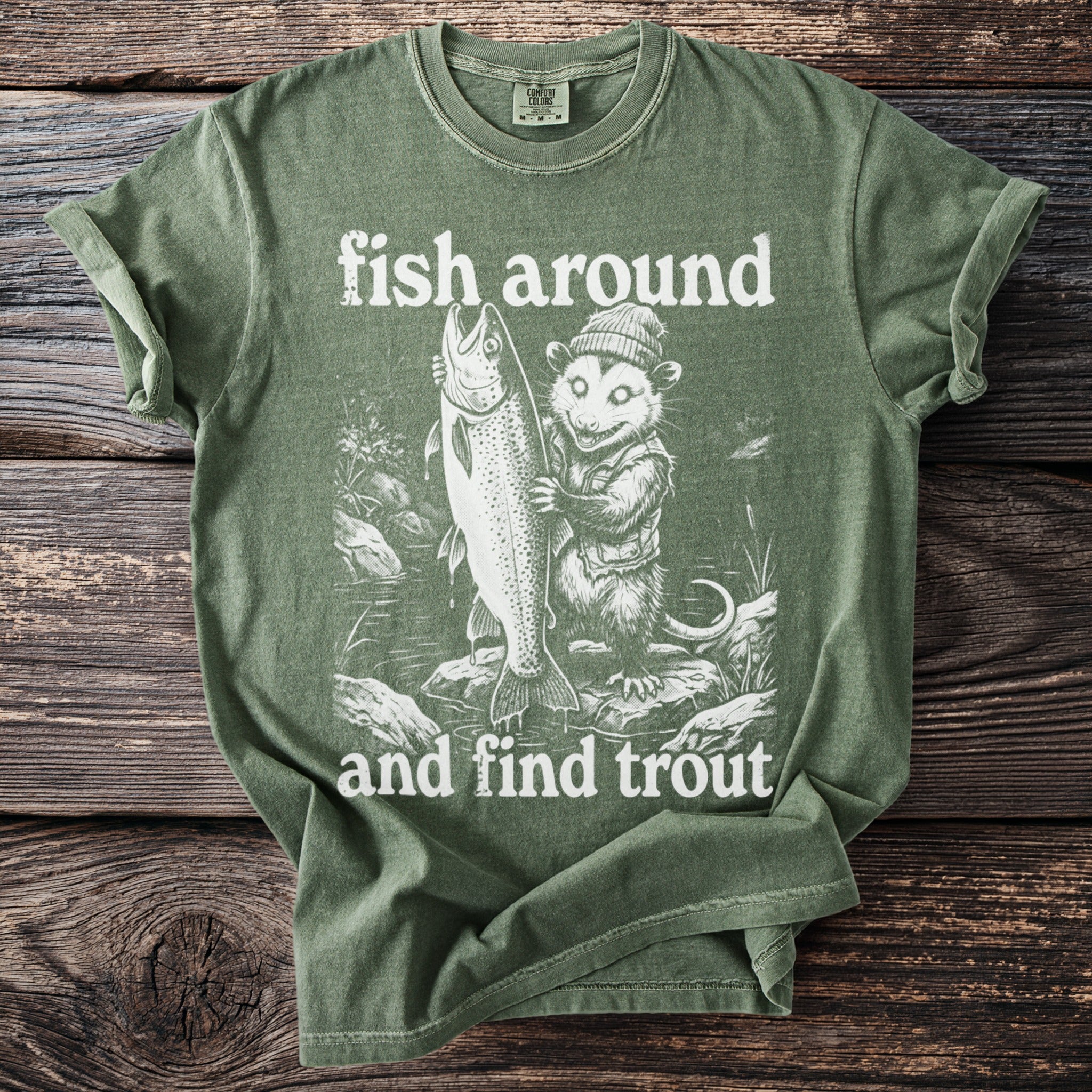 Green t-shirt graphic of possum holding large fish with text "fish around and find trout".