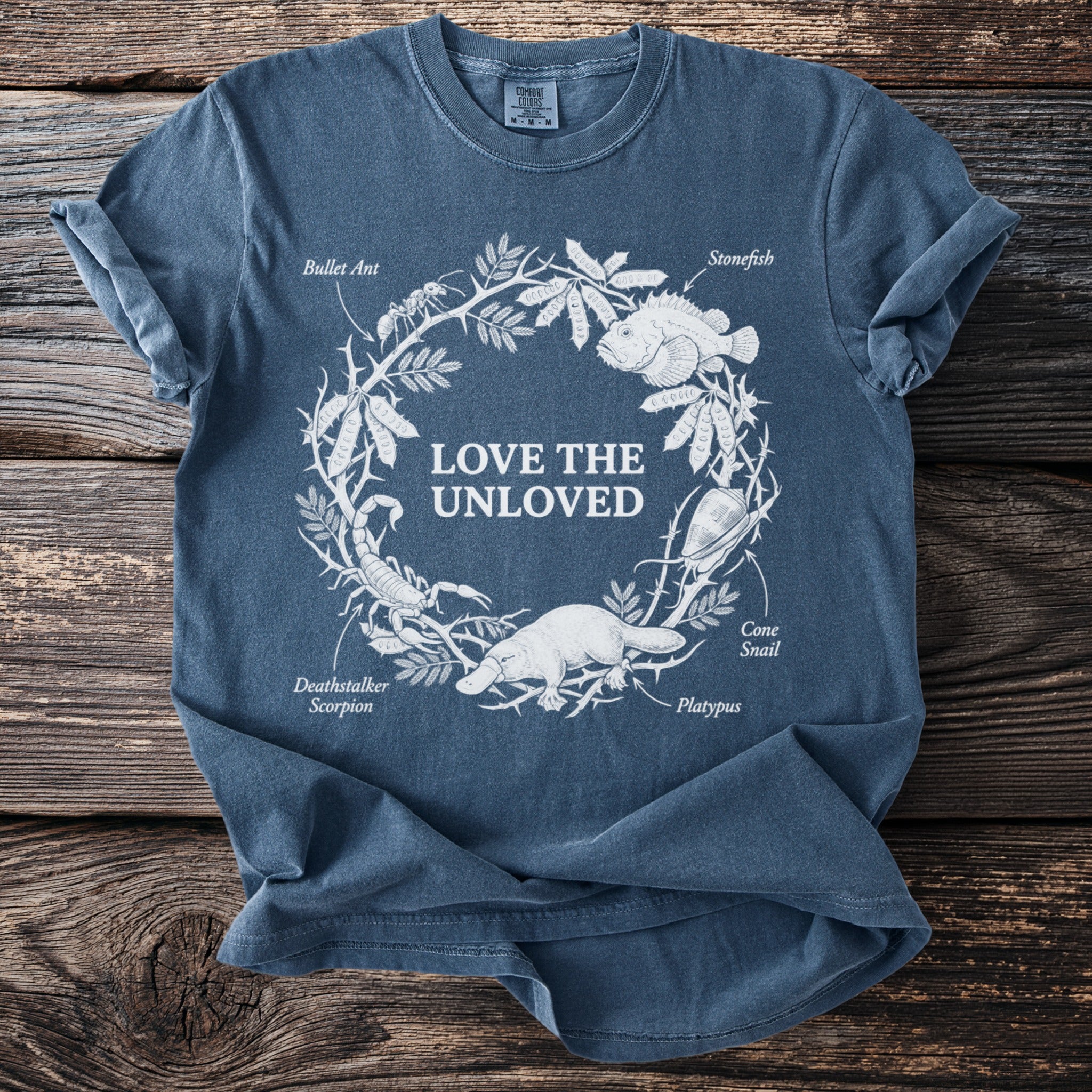 Blue t-shirt with "Love the Unloved" text and illustrations of animals from a nature wreath.