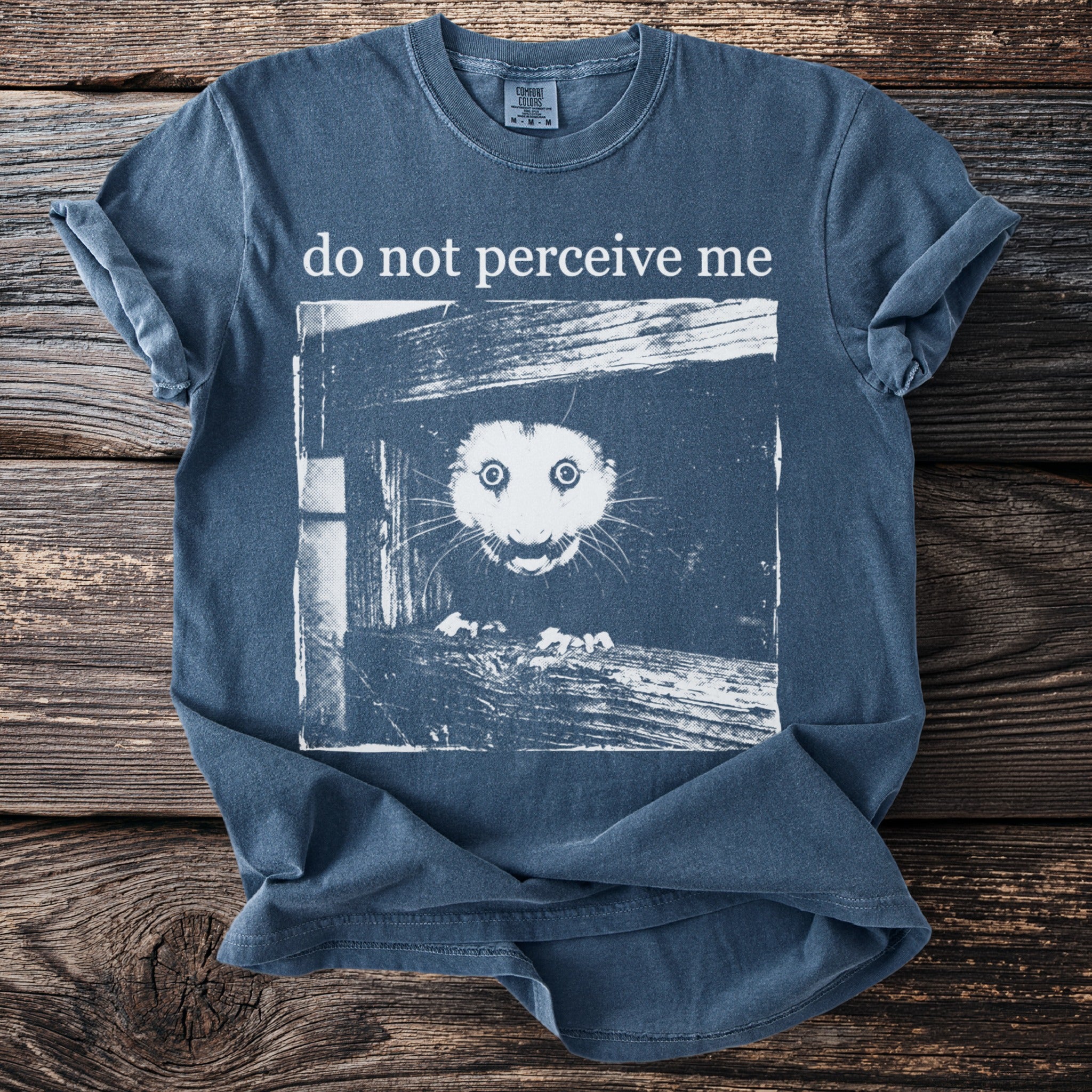 Blue T shirt with a bushbaby peering through wooden planks and “do not perceive me” text.