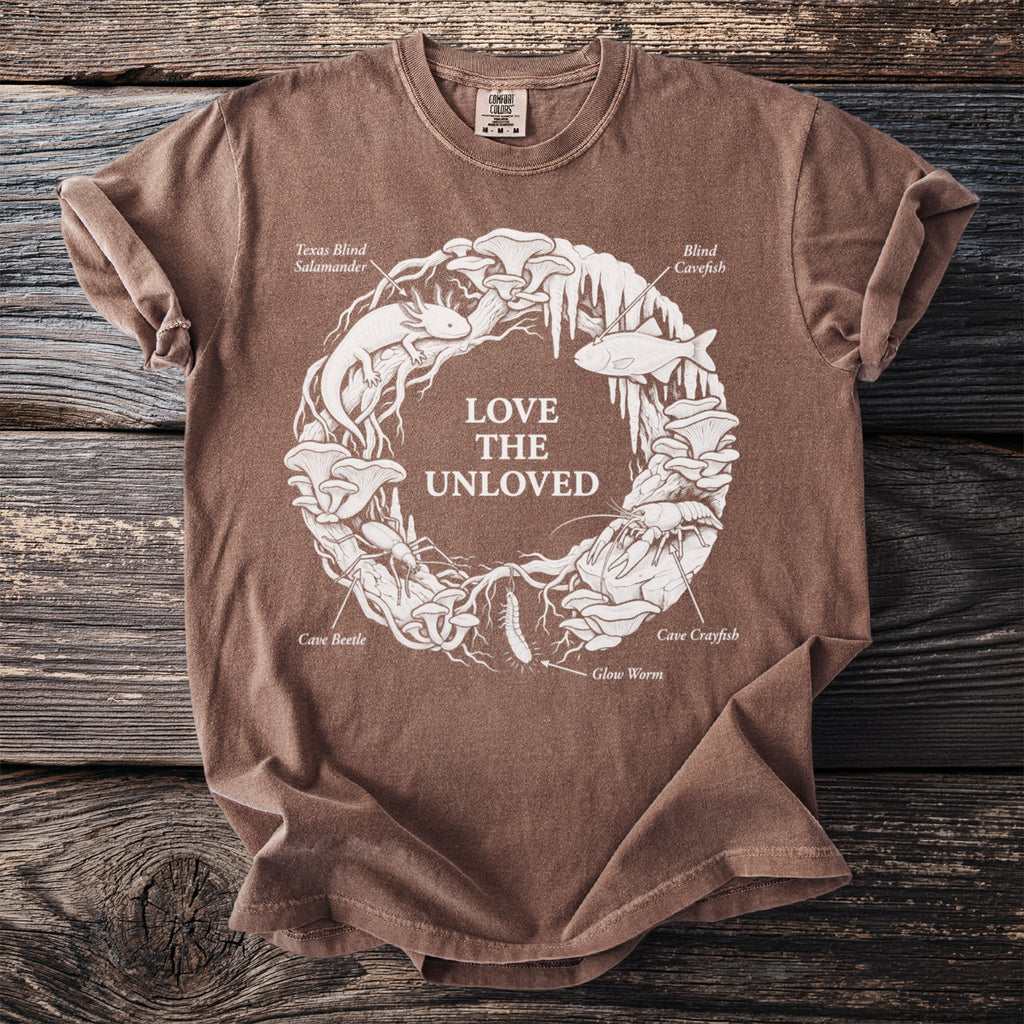 Brown t-shirt with circle design of cave creatures and plants, text "LOVE THE UNLOVED".