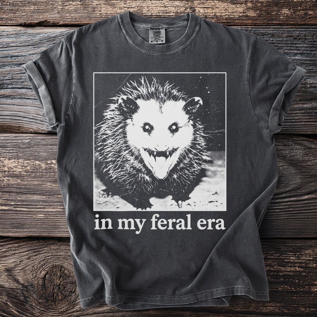 Dark t-shirt with a graphic of an opossum and text that reads "in my feral era".