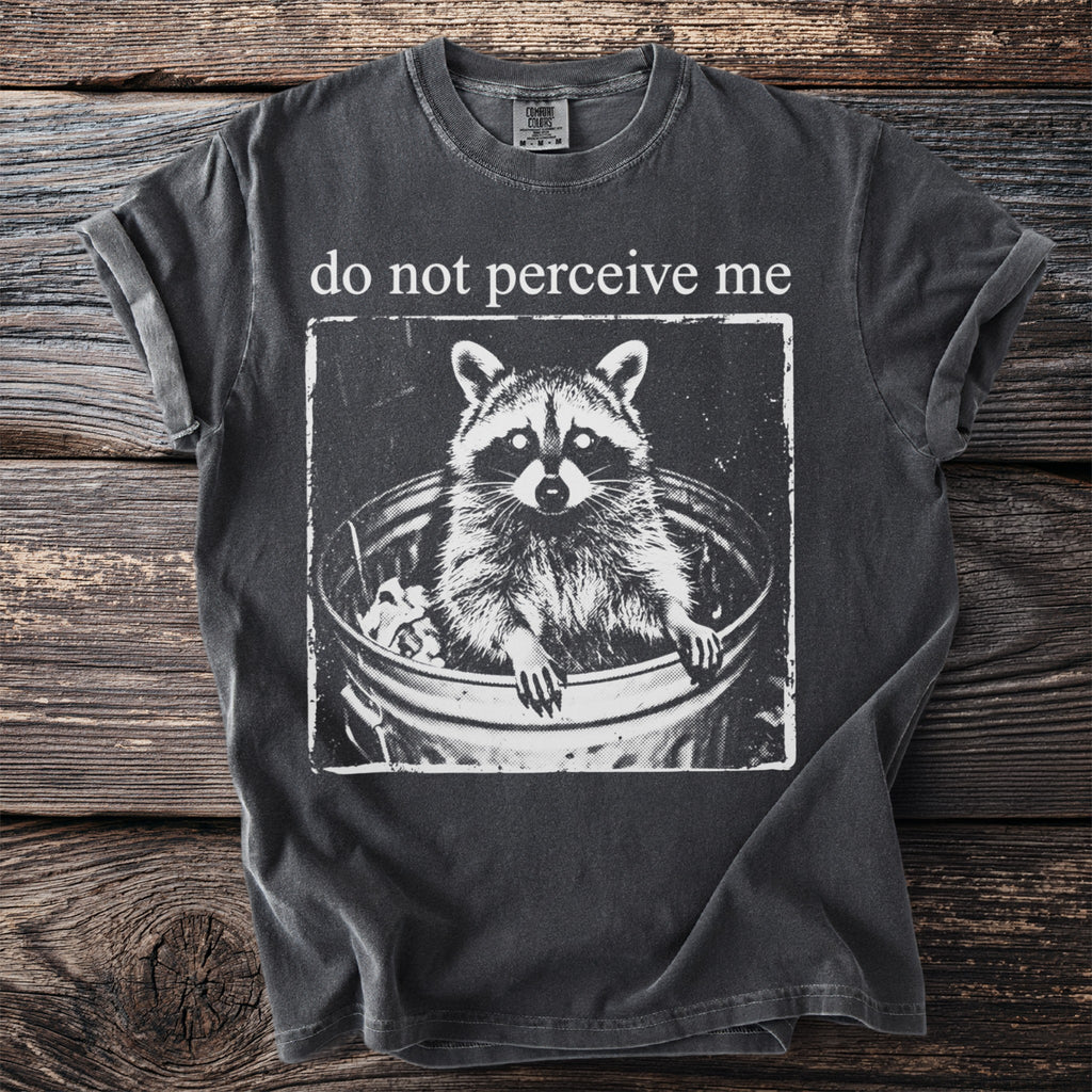 Dark grey t-shirt with a raccoon in a trash can graphic and text "do not perceive me".