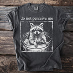 Dark grey t-shirt with a raccoon in a trash can graphic and text "do not perceive me".