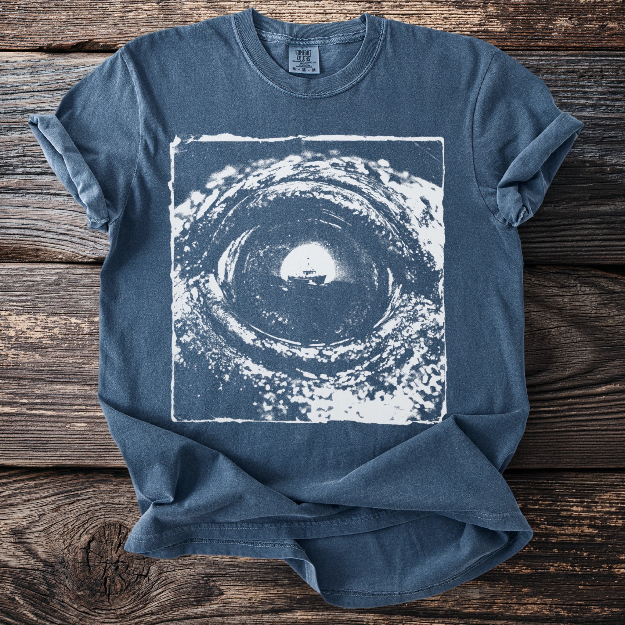 Blue t-shirt with a white distressed graphic of a boat in a swirling tunnel.