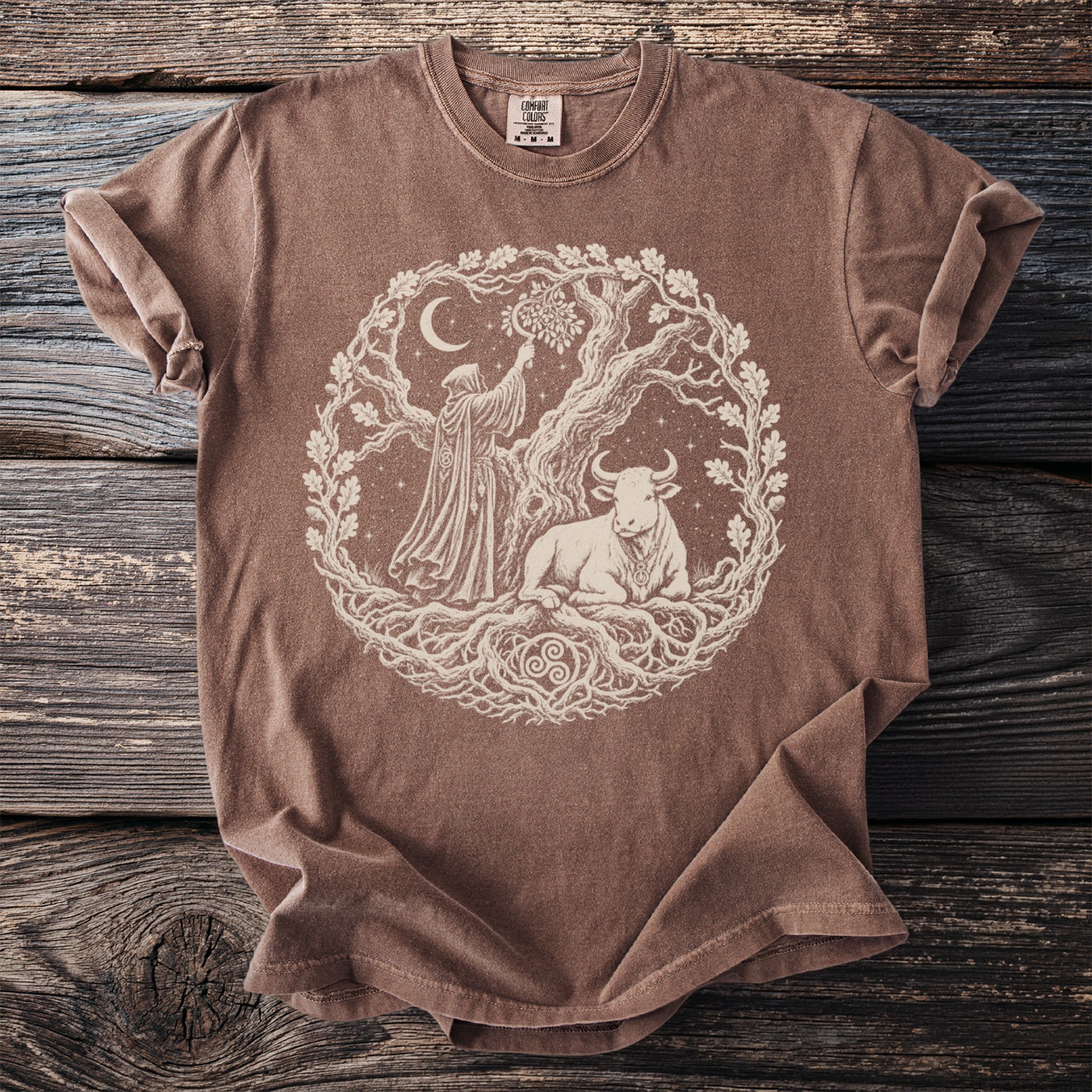 Brown t-shirt featuring a circular design of a robed figure, a bull, and a tree with ornate roots.