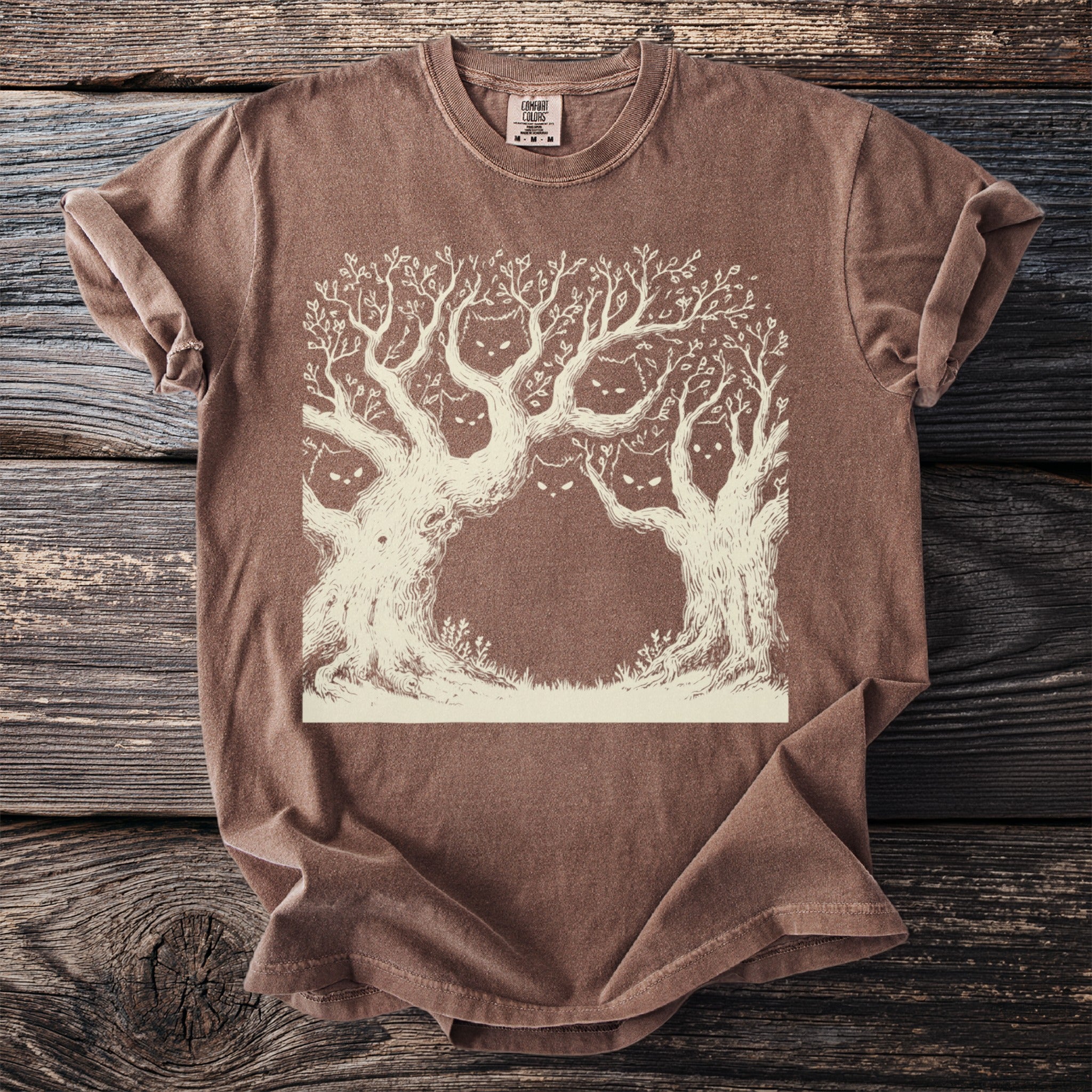 Brown t-shirt with a cream line drawing of spooky trees with cat faces.