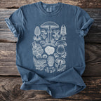 Blue t-shirt with white line art of various mushrooms and ferns on a wooden background.
